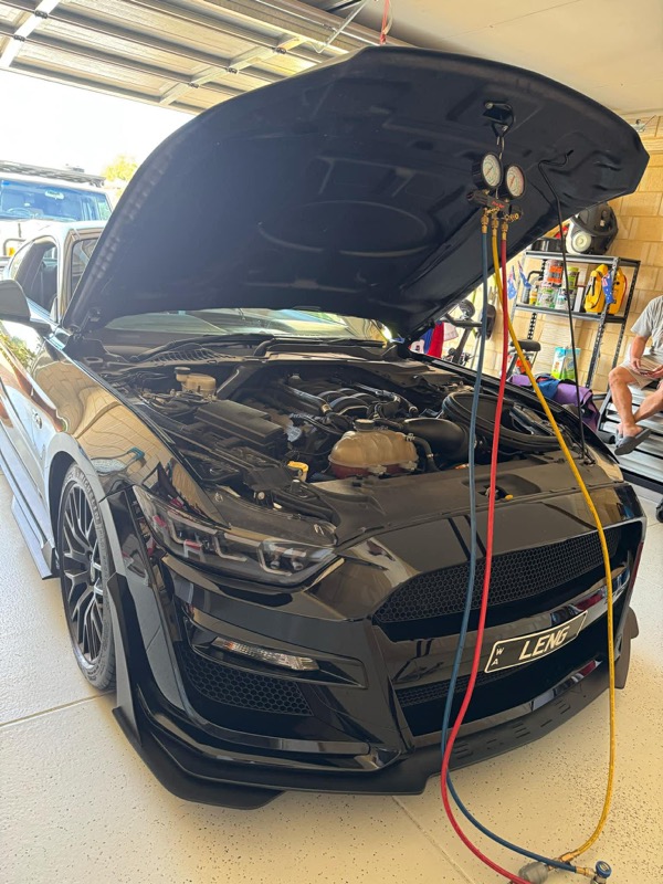 Black Ford Mustang with its bonnet open and air conditioning gauges connected in a workshop